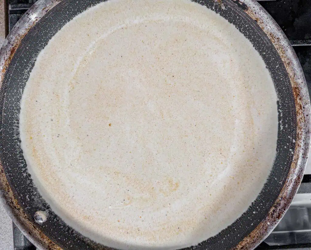 Thin pancake batter spread in a nonstick frying pan on a stovetop.