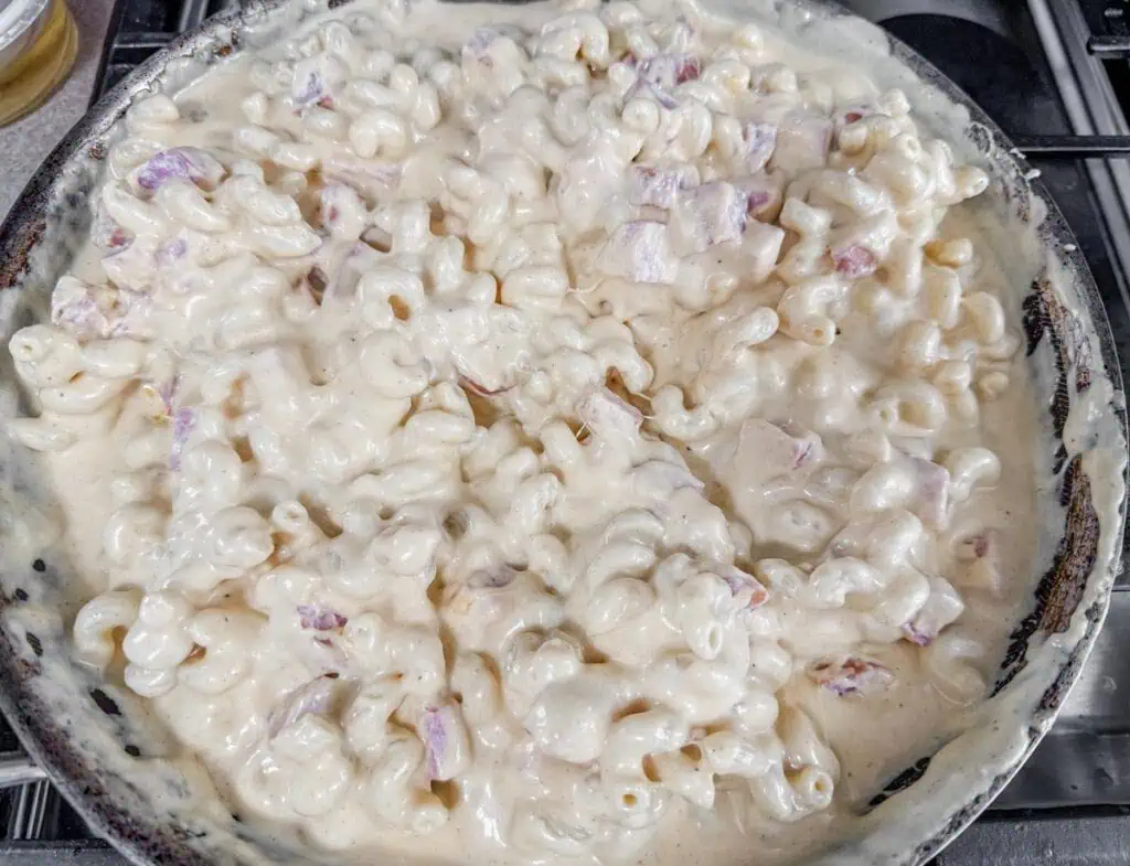 A pan filled with creamy macaroni and cheese mixed with diced purple onions.