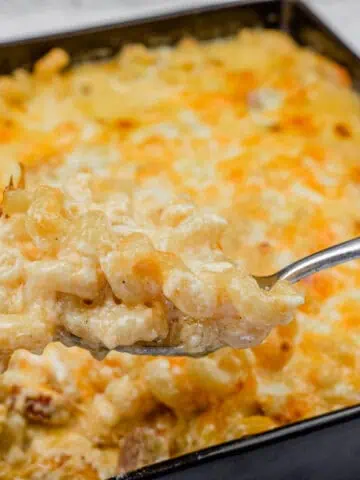A square casserole dish filled with baked macaroni and cheese, with a spoon holding a portion above it.