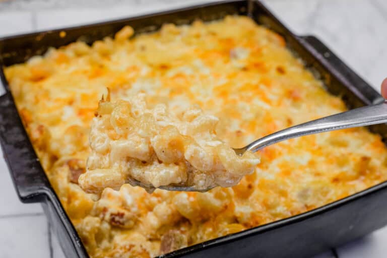 A square casserole dish filled with baked macaroni and cheese, with a spoon holding a portion above it.