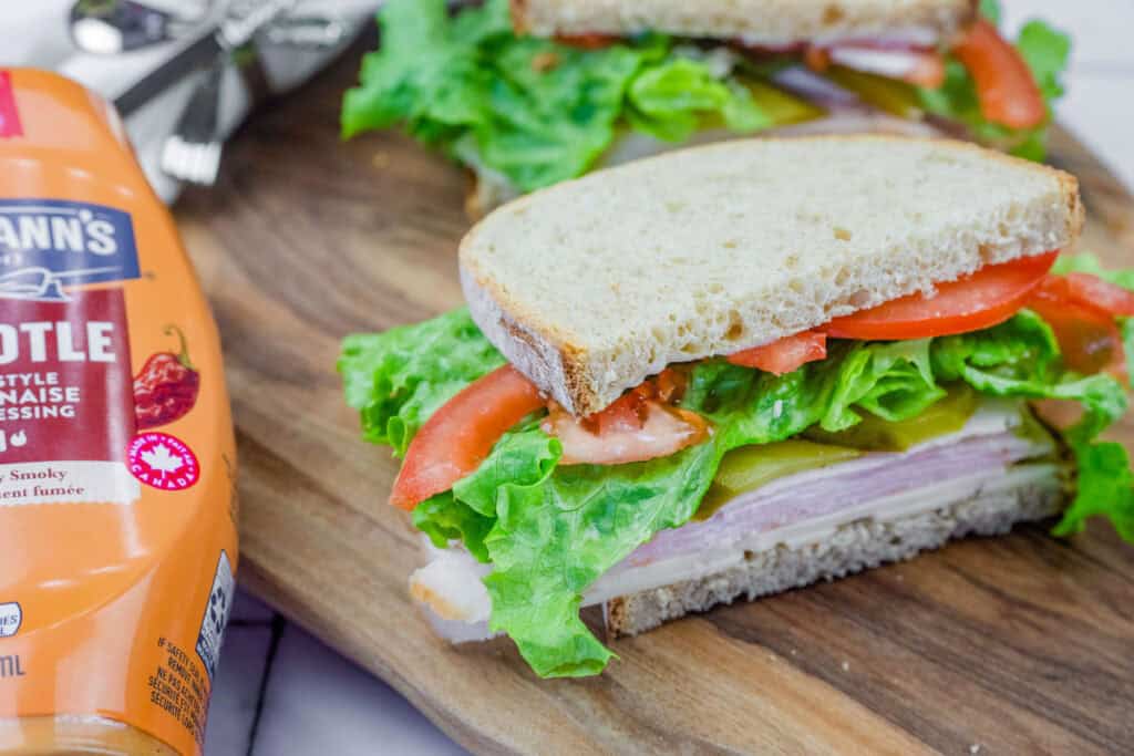 Turkey sandwich with lettuce, tomato, pickles, and cheese on whole-grain bread, with Hellmann's Chipotle mayo beside it.