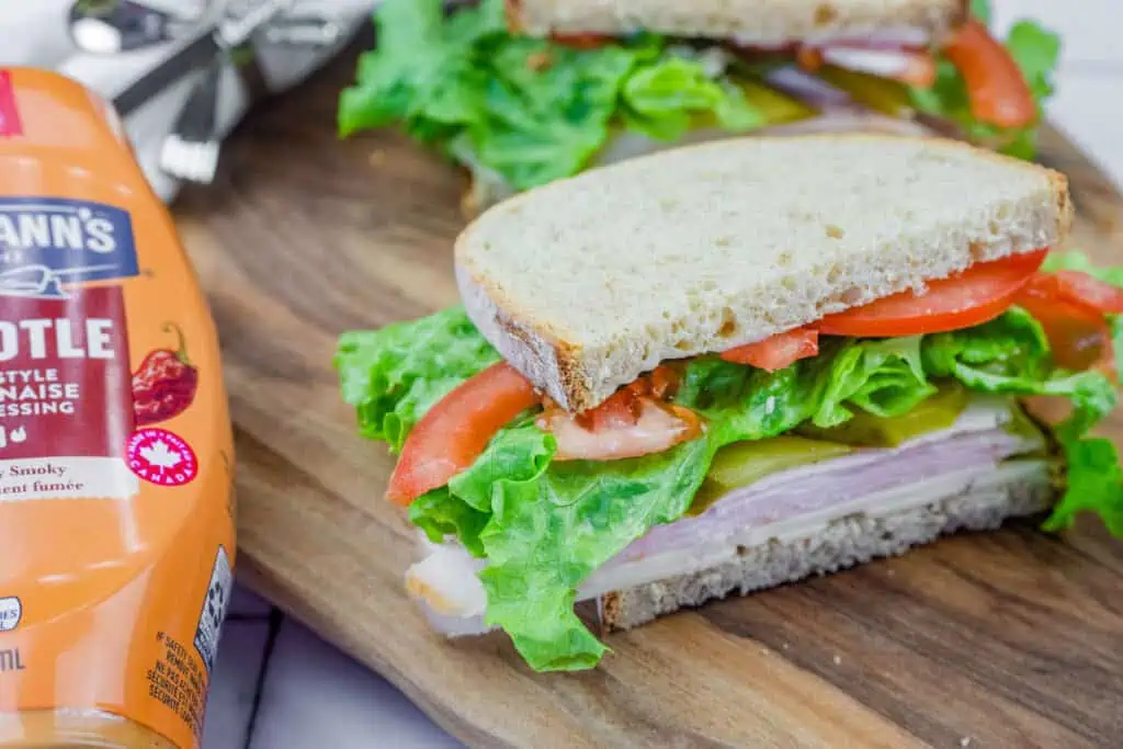 Turkey sandwich with lettuce, tomato, pickles, and cheese on whole-grain bread, with Hellmann's Chipotle mayo beside it.