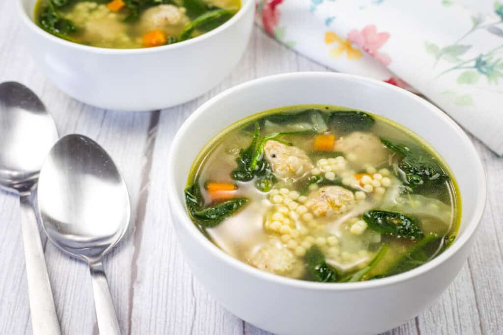 Two bowls of Italian Wedding Soup beside spoon and napkin.