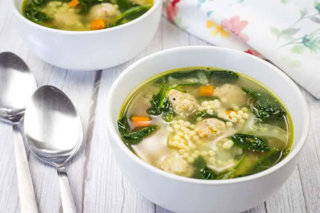 Two bowls of Italian Wedding Soup beside spoon and napkin.