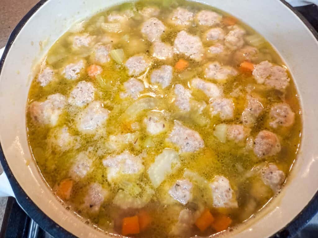 Homemade meatball soup simmering with broth, carrots, celery, and onions in a pot.