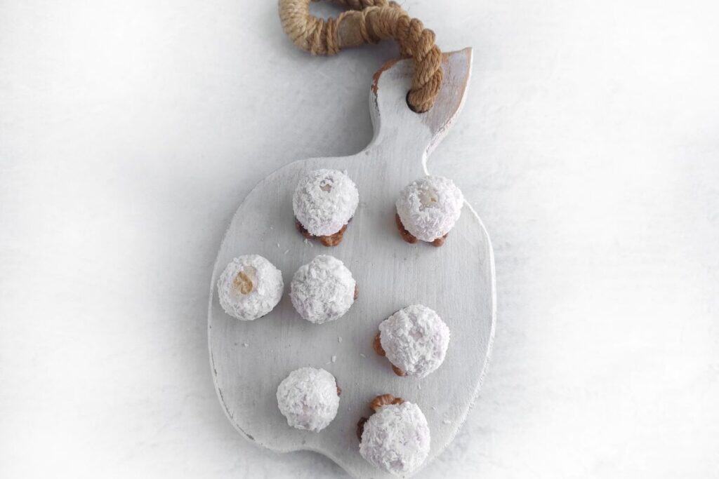 Six powdered sugar-covered cookies are arranged on a white cutting board with a rope handle, placed on a light surface.