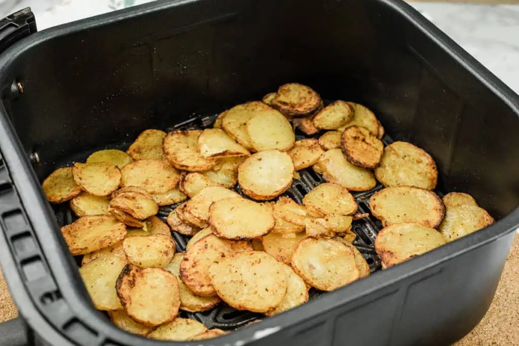 Slices of cooked potatoes in an air fryer basket.