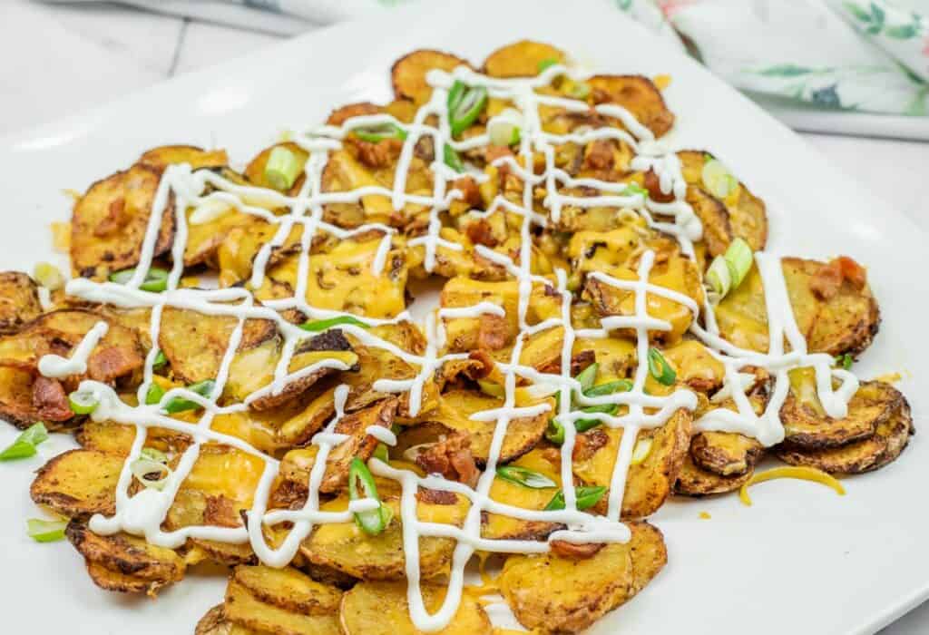 Air Fryer Irish Nachos topped with melted cheese, bacon bits, green onions, and drizzled with sour cream on a white plate.