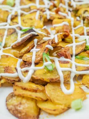 Sliced, roasted potatoes topped with melted cheese, bacon bits, green onions, and drizzled with mayonnaise.