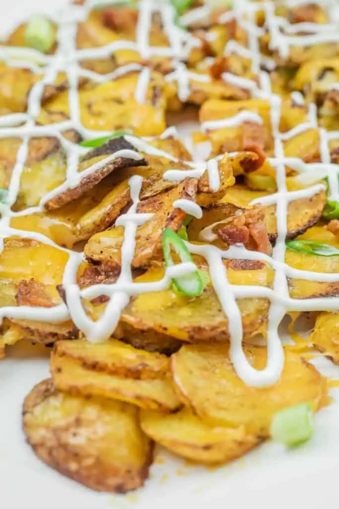 Sliced, roasted potatoes topped with melted cheese, bacon bits, green onions, and drizzled with mayonnaise.
