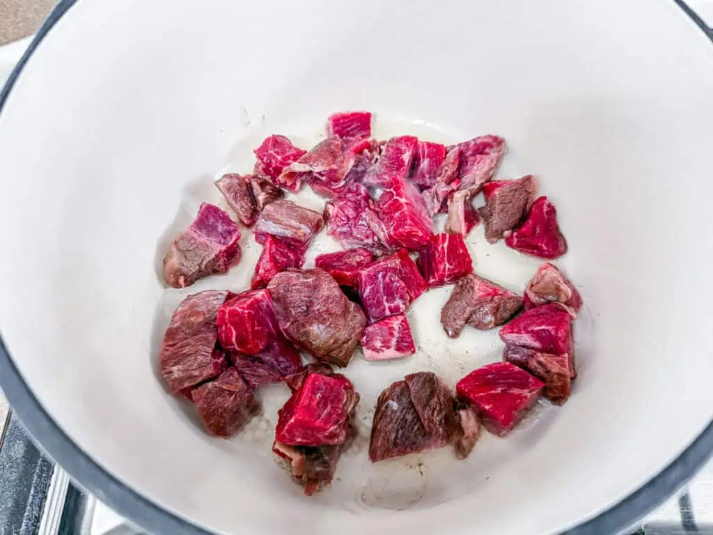 Cubed raw beef in a white pot, ready for cooking.