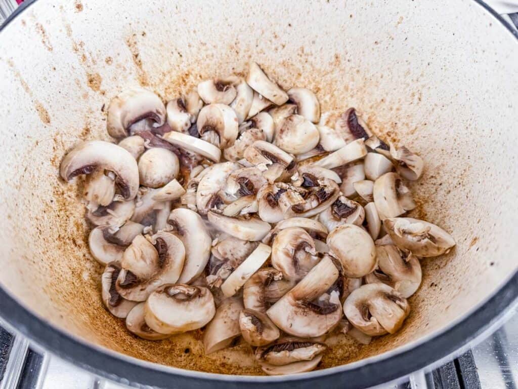 Sliced mushrooms being sautéed in a pot on a stove.