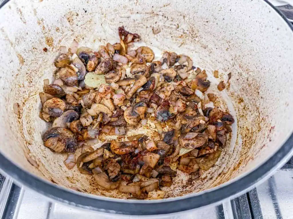Sautéed mushrooms and onions in a large pot on a stove.