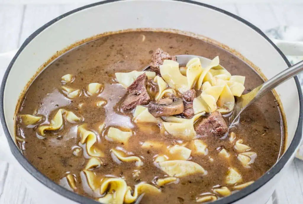 A pot of Beef Stroganoff Soup with visible chunks of beef and wide noodles in a dark broth.