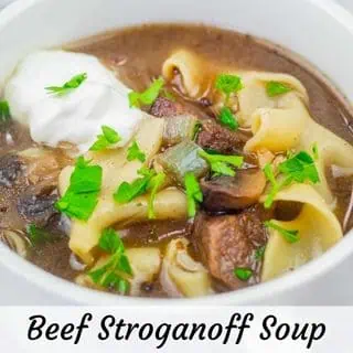 A white bowl of Beef Stroganoff Soup topped with sour cream and chopped parsley.