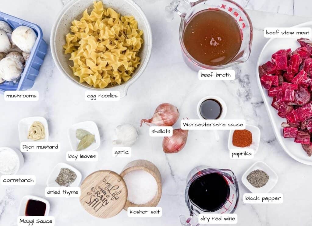 Ingredients for Beef Stroganoff Soup laid out: mushrooms, egg noodles, beef stew meat, beef broth, shallots, Worcestershire sauce, paprika, black pepper, dry red wine, kosher salt, thyme, cornstarch, bay leaves.