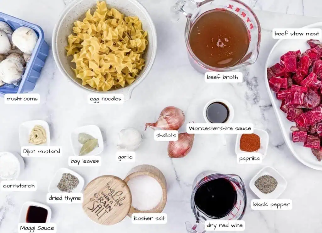 Ingredients for Beef Stroganoff Soup laid out: mushrooms, egg noodles, beef stew meat, beef broth, shallots, Worcestershire sauce, paprika, black pepper, dry red wine, kosher salt, thyme, cornstarch, bay leaves.