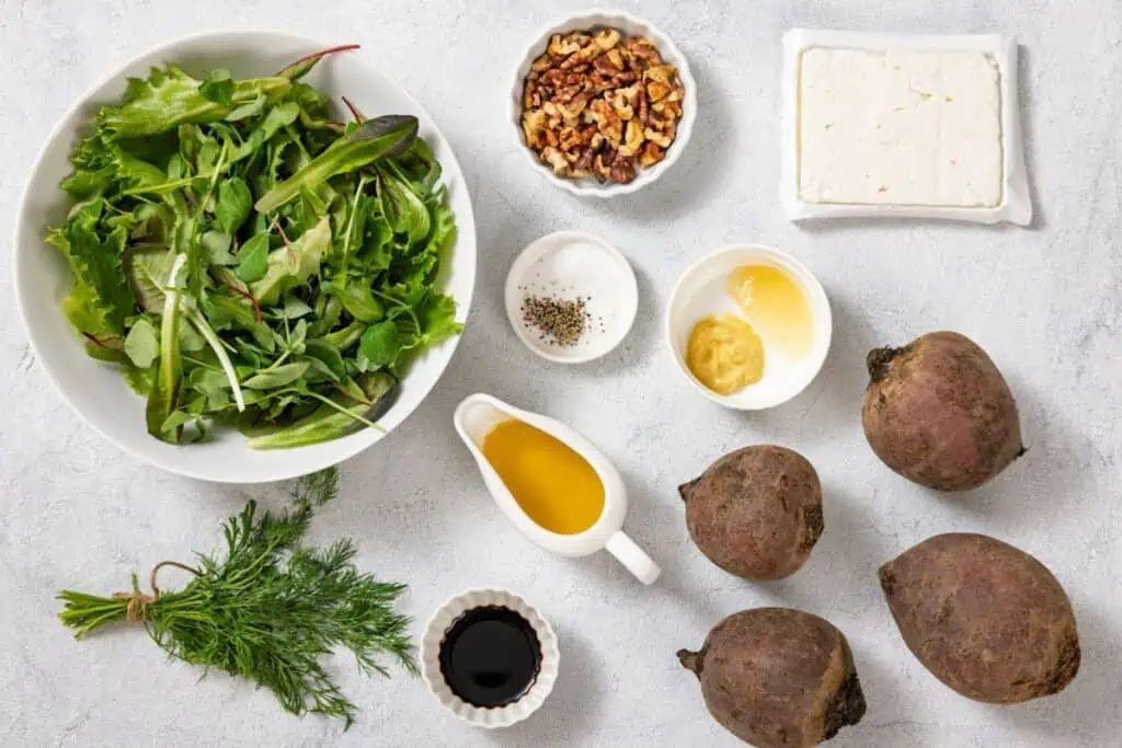 Ingredients arranged on a surface: leafy greens, walnuts, feta, beets, dill, olive oil, vinegar, salt, pepper, mustard, honey.