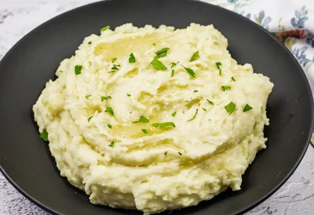 A black bowl filled with Grandma's Mashed Potatoes topped with chopped parsley.