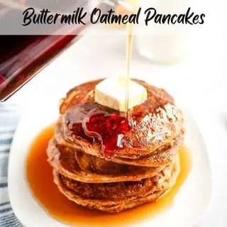 Stack of buttermilk oatmeal pancakes topped with butter and syrup being poured, on a white plate with a striped cloth underneath.