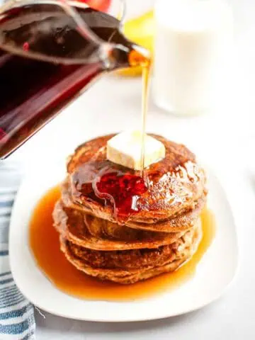 Syrup is poured onto a stack of Buttermilk Oatmeal Pancakes topped with a pat of butter.