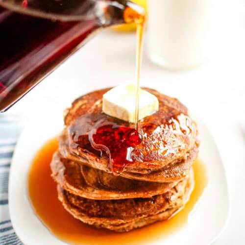 Syrup is poured onto a stack of Buttermilk Oatmeal Pancakes topped with a pat of butter.