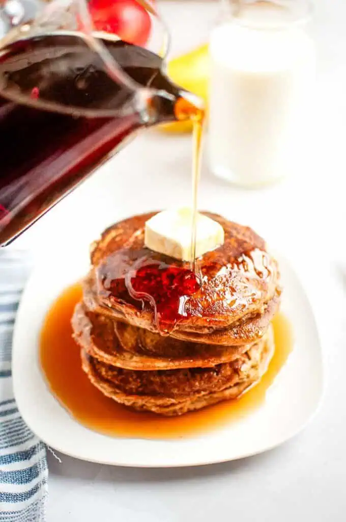 Syrup is poured onto a stack of Buttermilk Oatmeal Pancakes topped with a pat of butter.