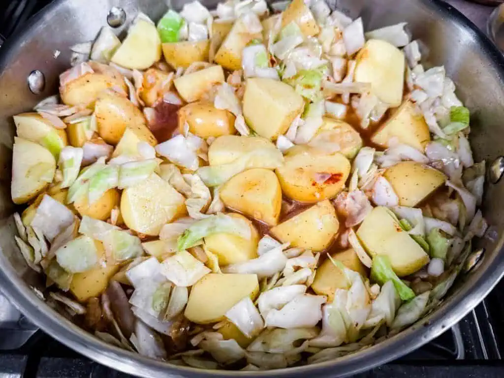 Chopped cabbage and potatoes in a pot with seasoning, ready for cooking.