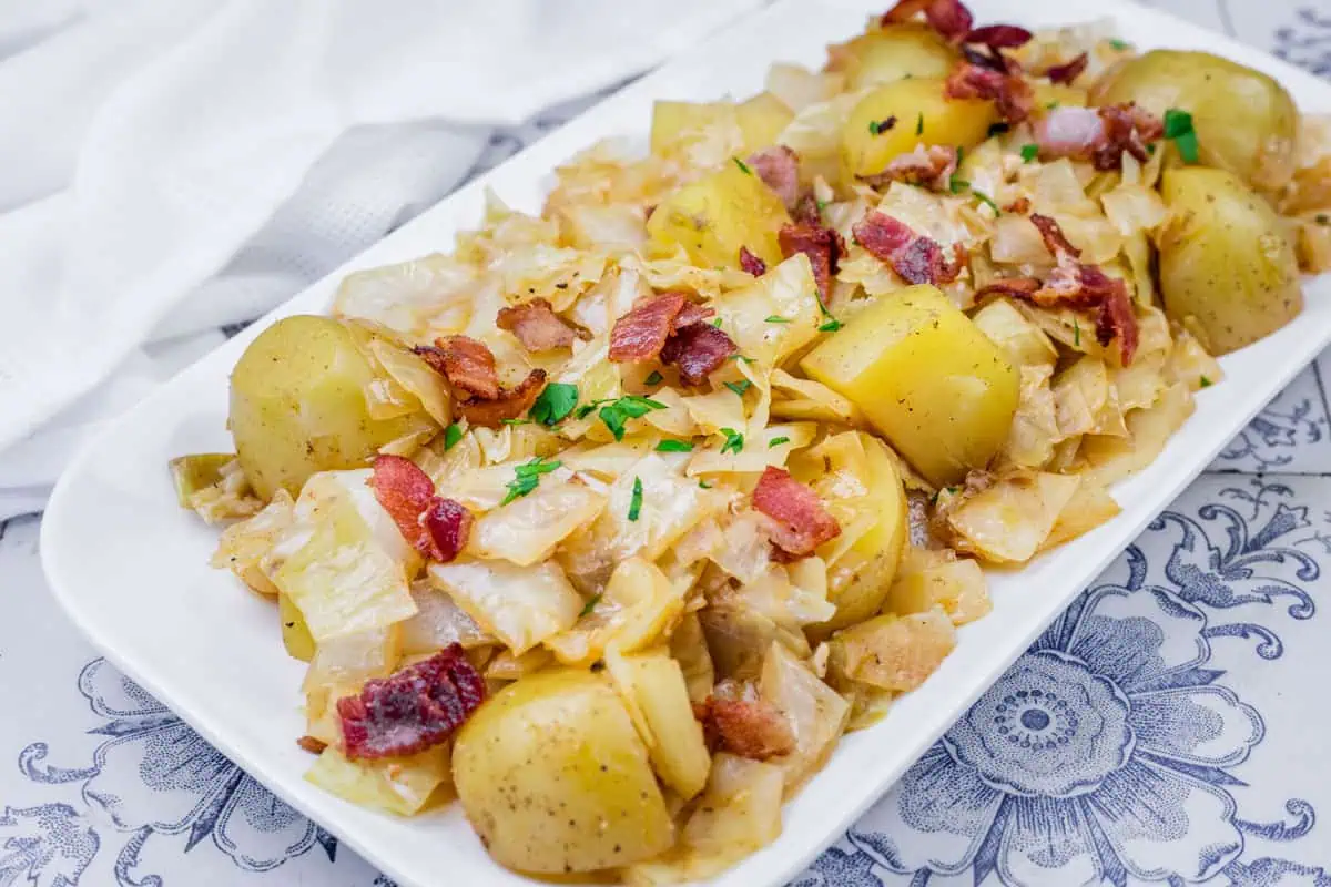 A white rectangular plate with Potatoes & Cabbage garnished with parsley on a patterned surface.