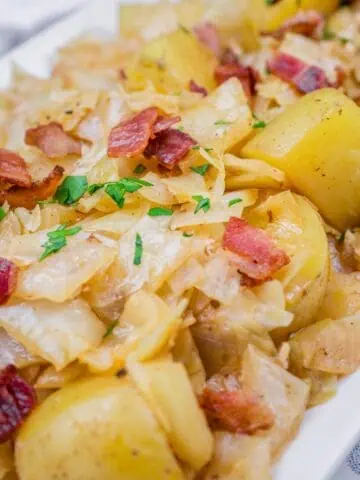 Savory sautéed Cabbage & Potatoes with Bacon, garnished with fresh parsley on a white serving dish.