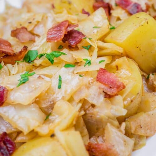 Savory saut&eacute;ed Cabbage & Potatoes with Bacon, garnished with fresh parsley on a white serving dish.