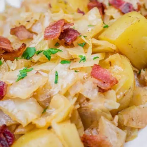 Savory sautéed Cabbage & Potatoes with Bacon, garnished with fresh parsley on a white serving dish.