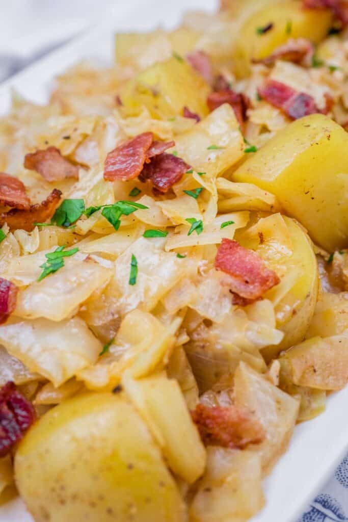 Savory saut&eacute;ed Cabbage & Potatoes with Bacon, garnished with fresh parsley on a white serving dish.