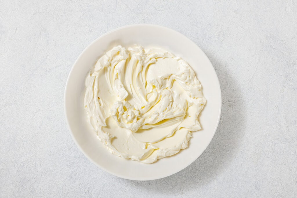 A bowl filled with creamy white cream cheese on a light gray surface.