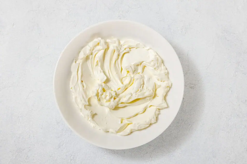 A bowl filled with creamy white cream cheese on a light gray surface.