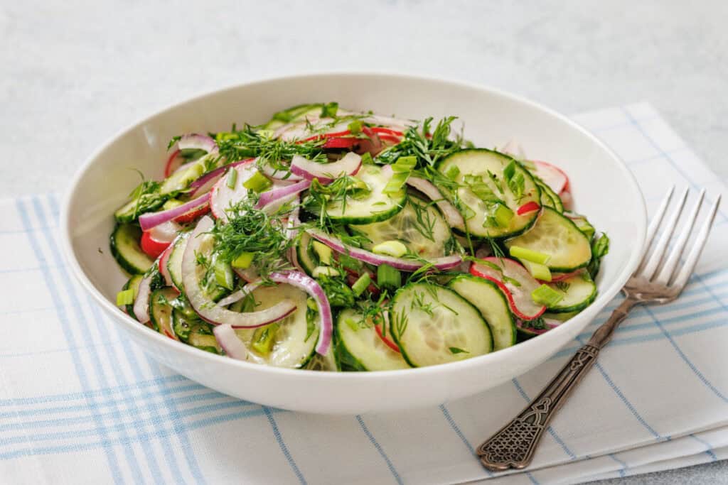 A bowl of Radish Salad with sliced red onions, radishes, and herbs on a cloth napkin with a fork beside it.