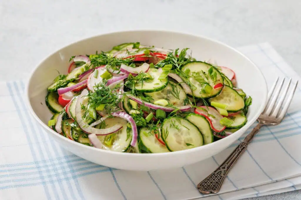 A bowl of Radish Salad with sliced red onions, radishes, and herbs on a cloth napkin with a fork beside it.