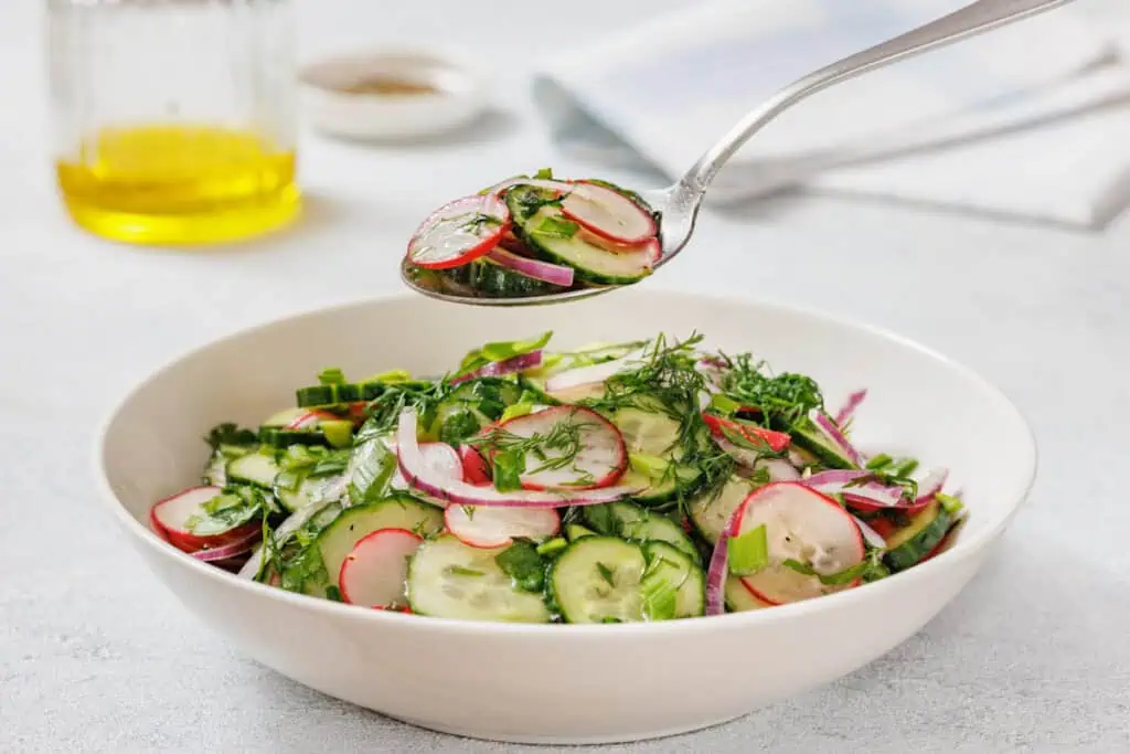 A bowl of Radish Salad garnished with herbs. A spoon holds a portion above the bowl.