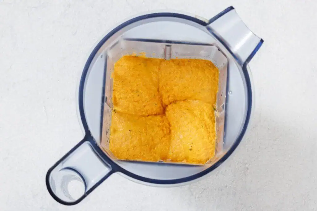 A blender with an orange mixture inside, viewed from above. The blender is on a light surface.