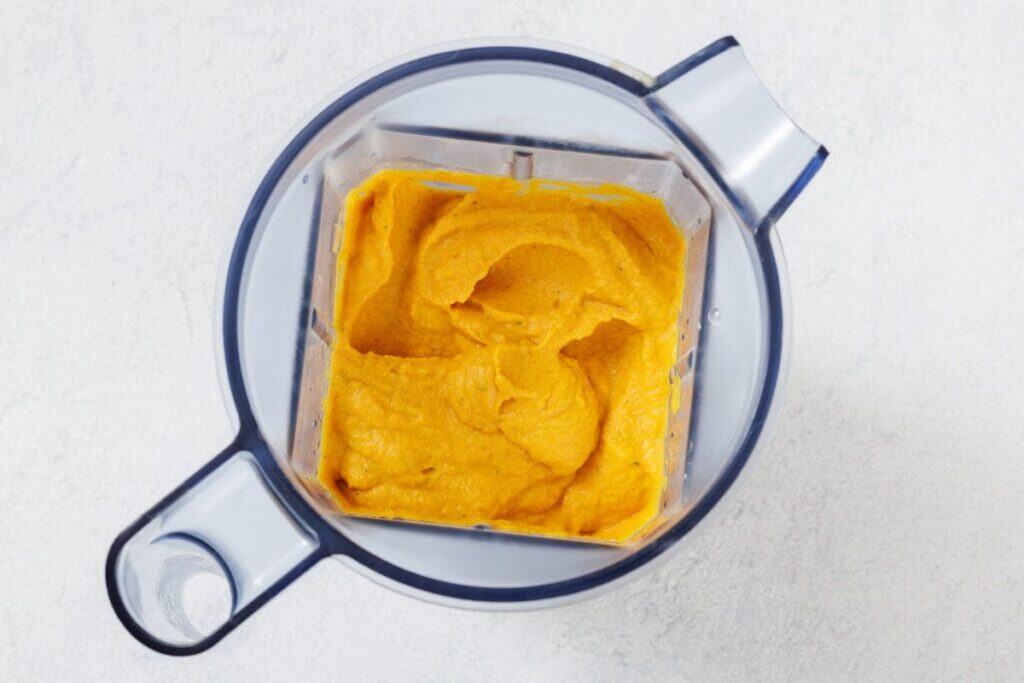 A blender filled with smooth, orange-colored puree sits on a white surface, viewed from above.