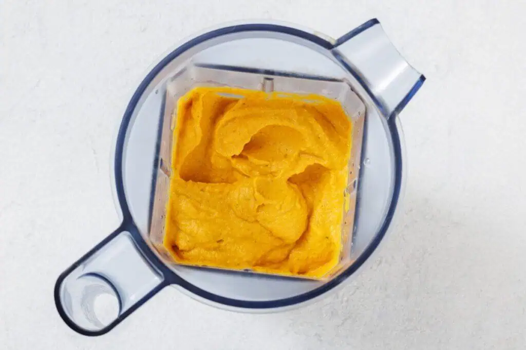 A blender filled with smooth, orange-colored puree sits on a white surface, viewed from above.