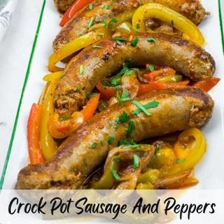 Slow Cooker Sausage & Peppers on a rectangular plate with sliced red, yellow, and green bell peppers, garnished with chopped herbs.