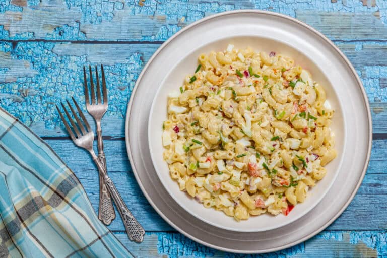 Plate of Deviled Egg Pasta Salad on a wooden table, accompanied by three forks and a blue plaid napkin.