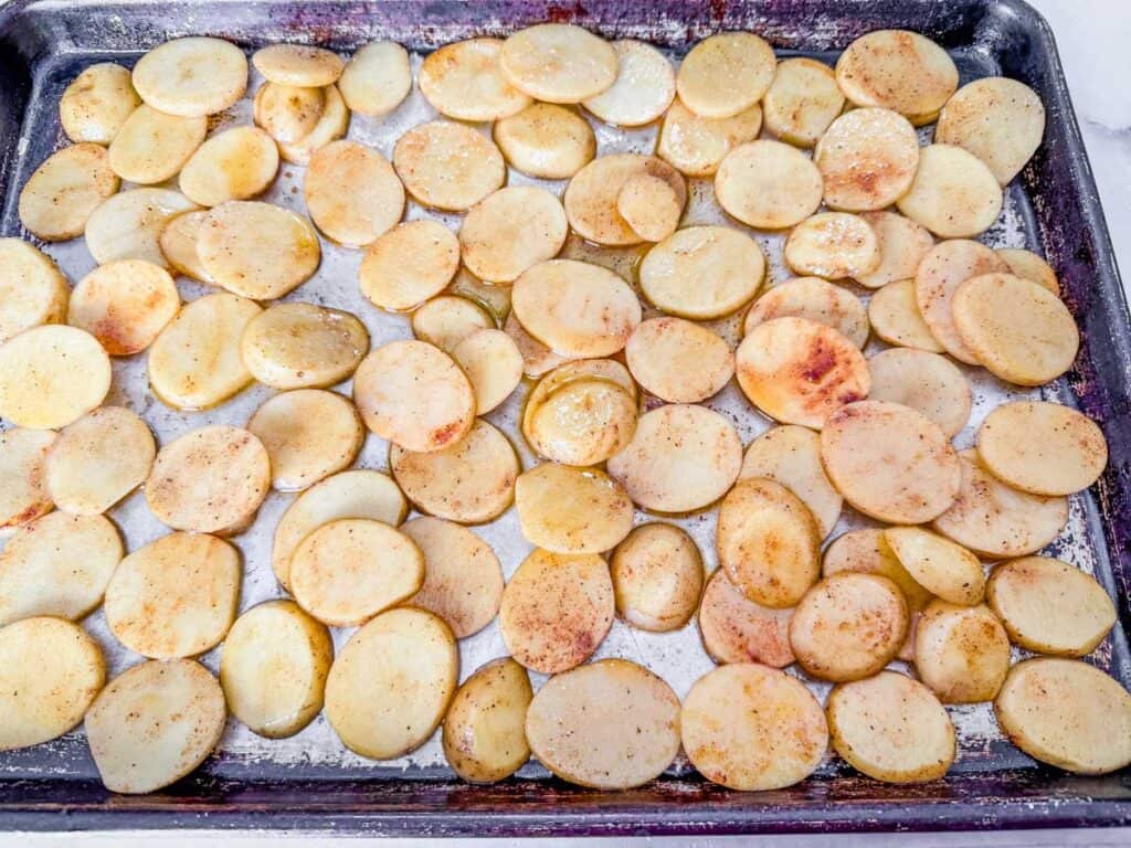 Sliced potatoes seasoned with spices are spread out on a baking sheet.