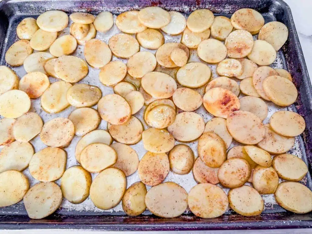 Sliced potatoes seasoned with spices are spread out on a baking sheet.