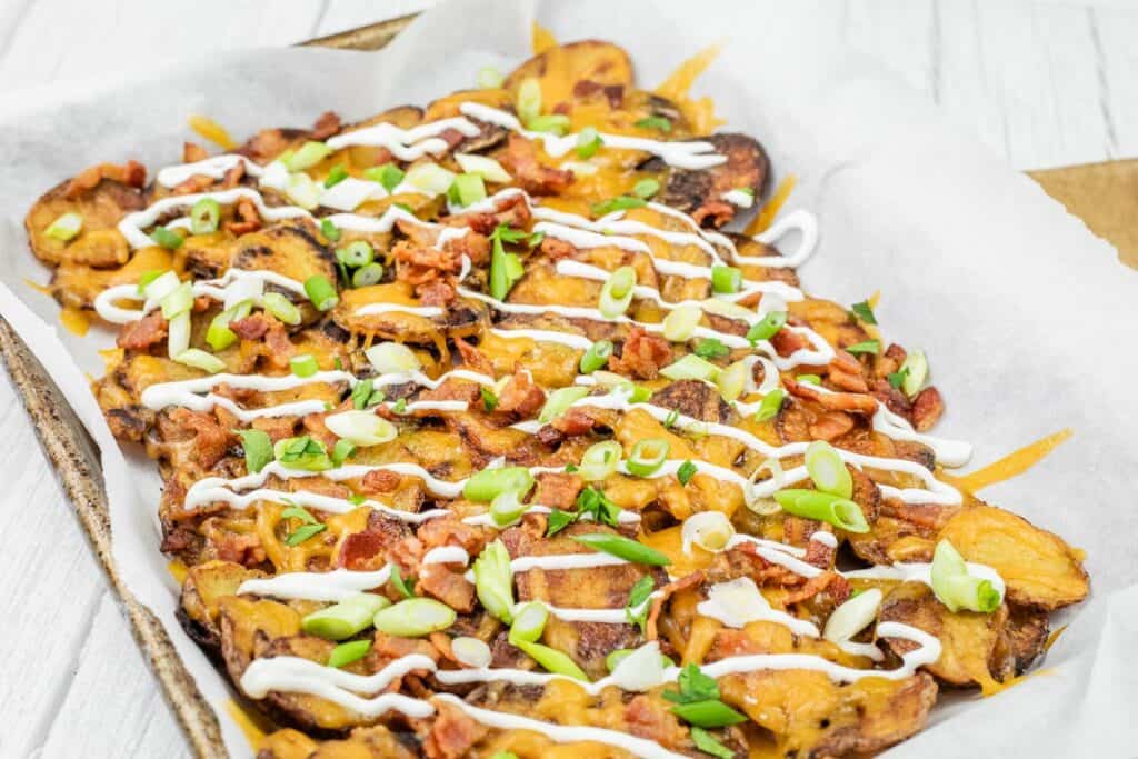A tray of loaded Irish nachos topped with melted cheese, green onions, bacon, and drizzled with sour cream.