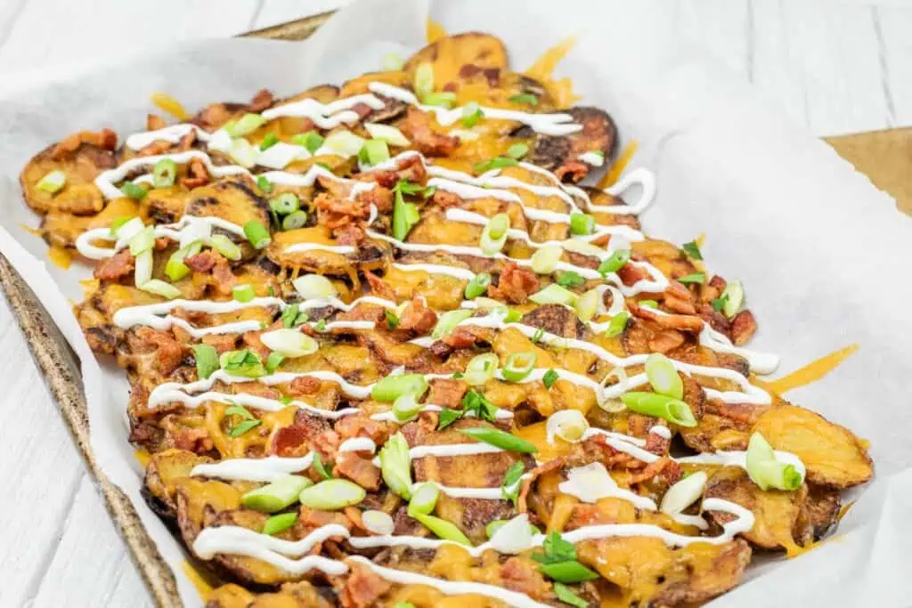 A tray of loaded Irish nachos topped with melted cheese, green onions, bacon, and drizzled with sour cream.