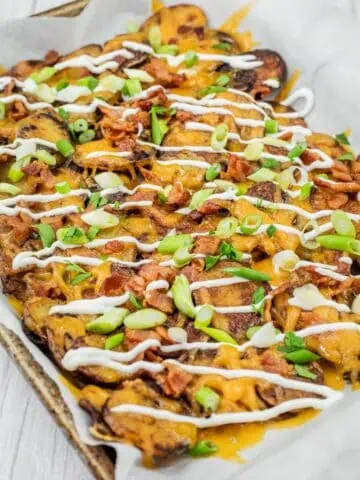 A tray of loaded Irish nachos topped with melted cheese, bacon, sliced green onions, and drizzled with sour cream.