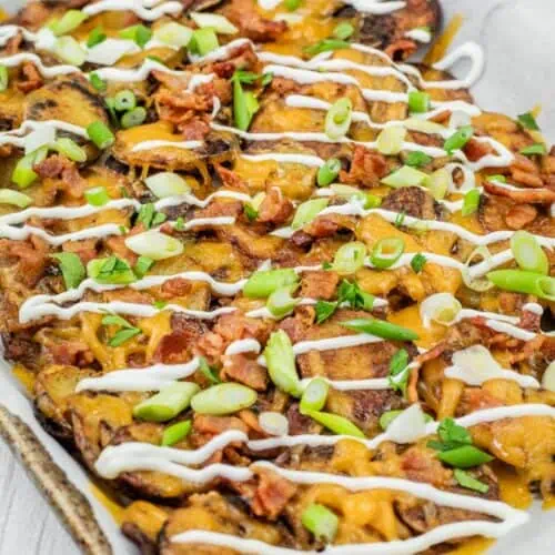 A tray of loaded Irish nachos topped with melted cheese, bacon, sliced green onions, and drizzled with sour cream.
