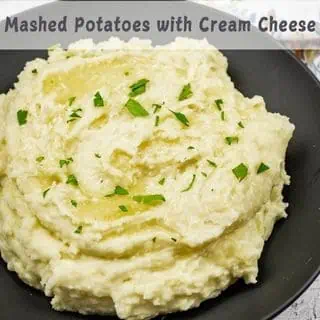 A black bowl filled with Grandma's Mashed Potatoes topped with chopped parsley.